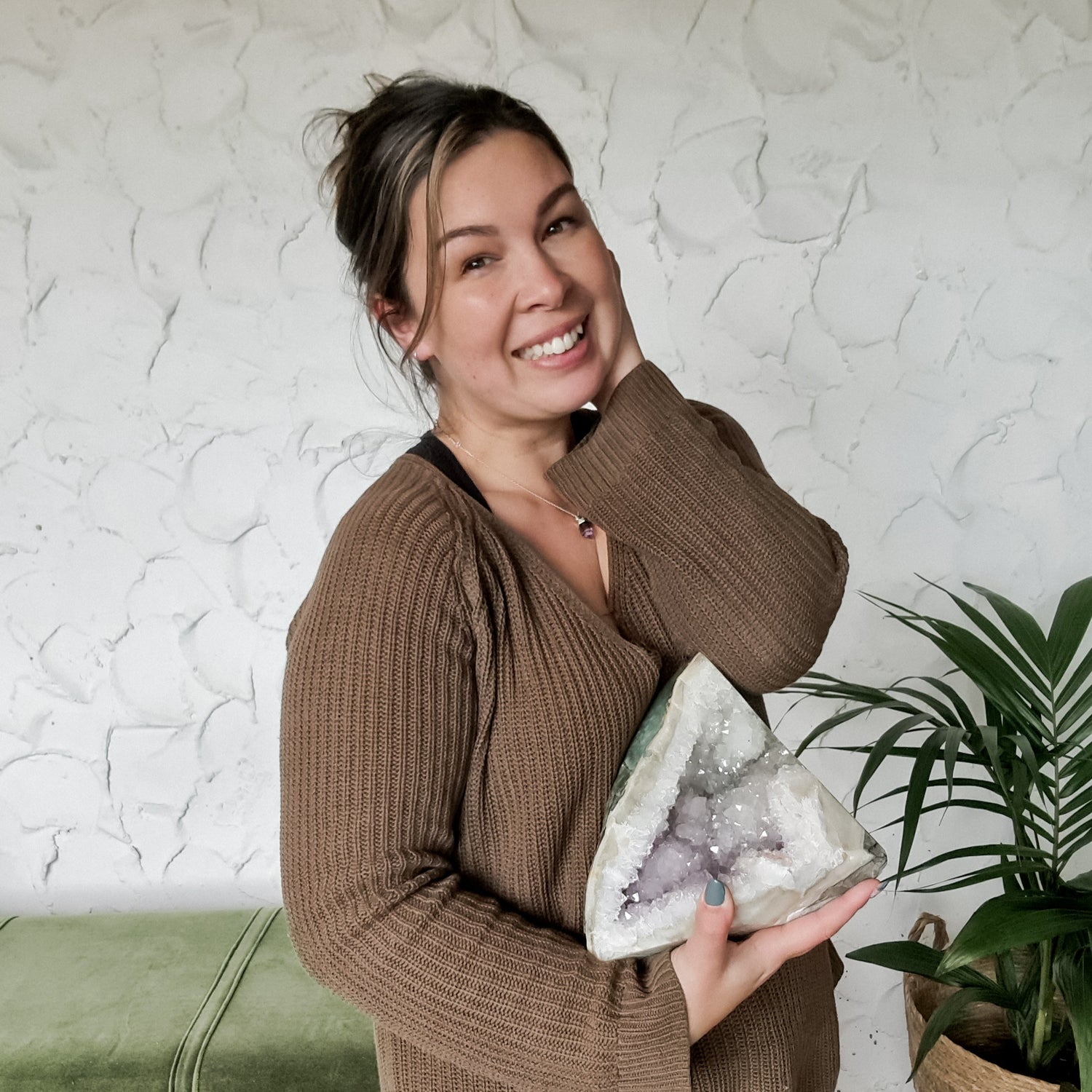 Woman holding a crystal rock in a cozy indoor setting with a plant and bench.