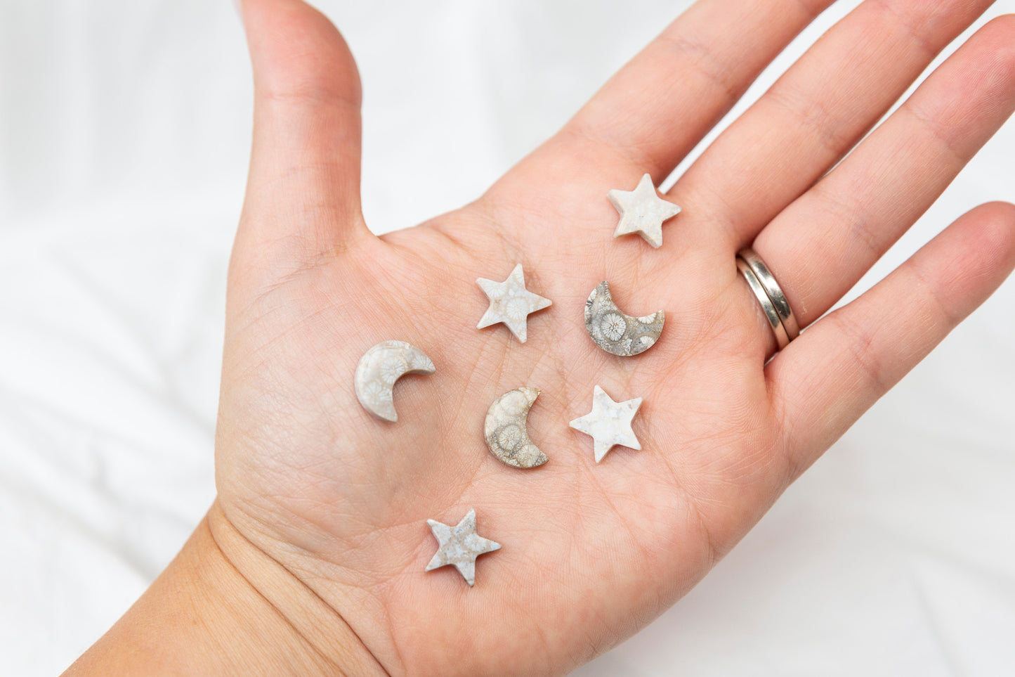 Hand holding small star and moon-shaped crystals against a white background