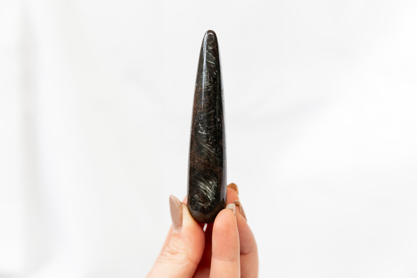 Hand holding a black stone tool against a white background