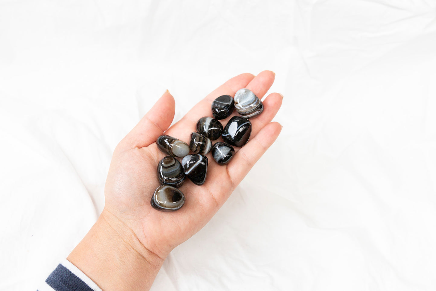 Hand holding black agate tumblestones against a white background