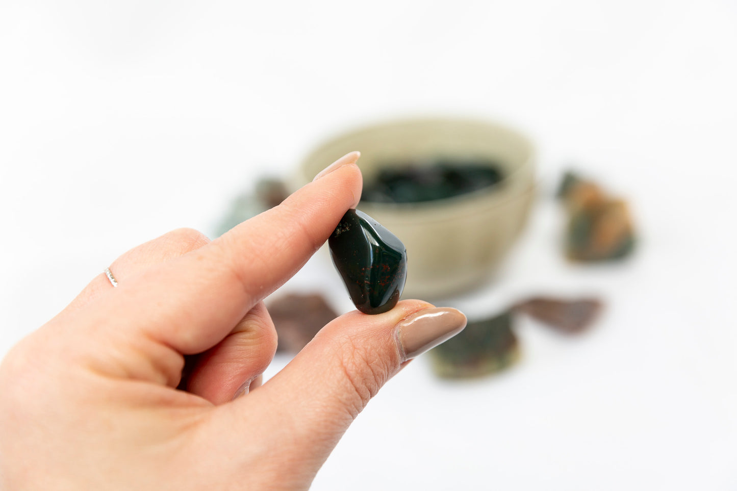 Hand holding a bloodstone crystal tumblestone with a blurred background