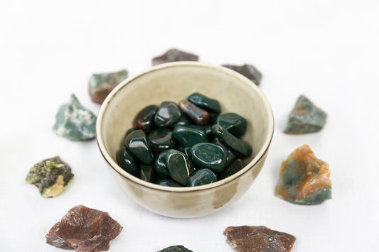 Small bowl filled with dark green stones on a white background