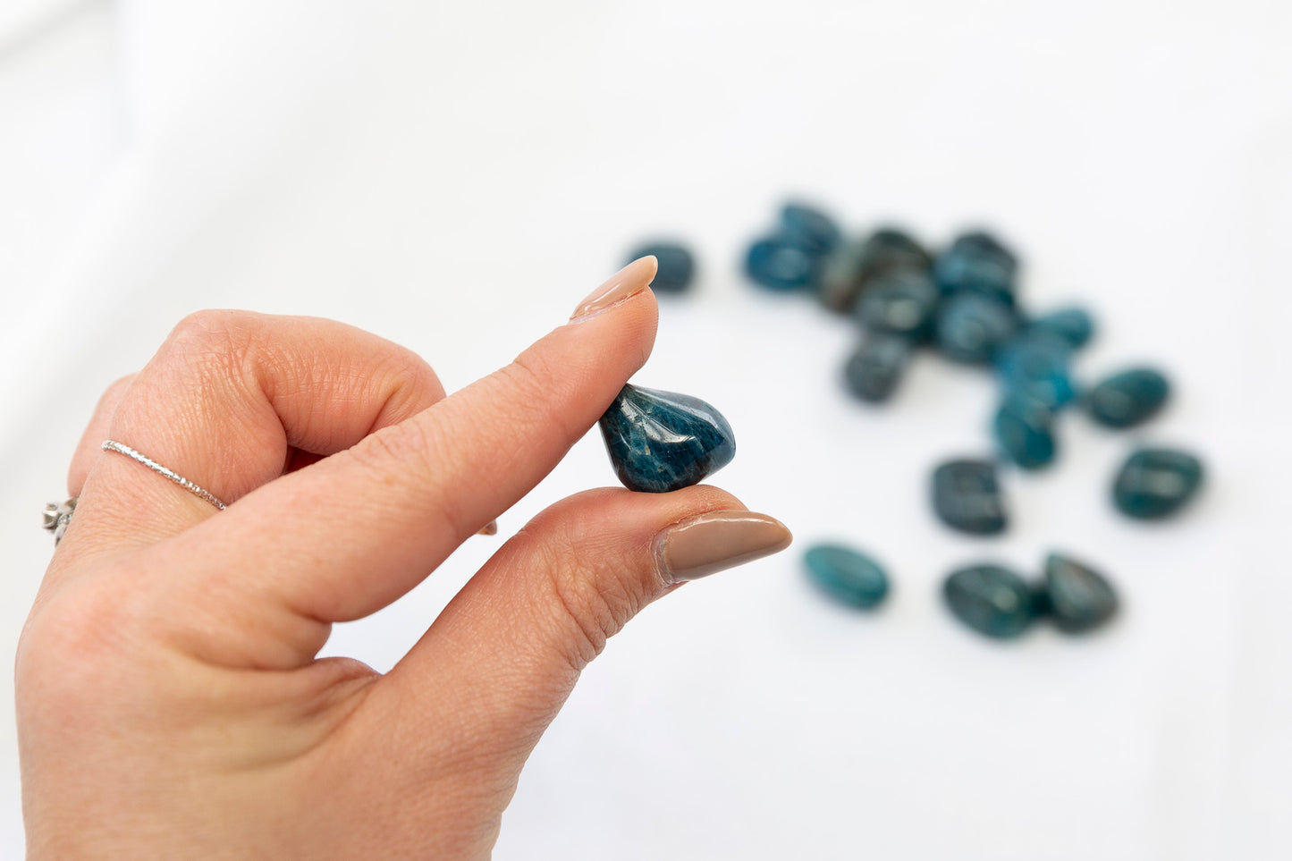 Hand holding a blue stone with more stones on a white background
