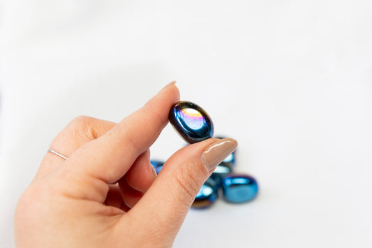 Hand holding a small, round, aura coated crystal against a white background