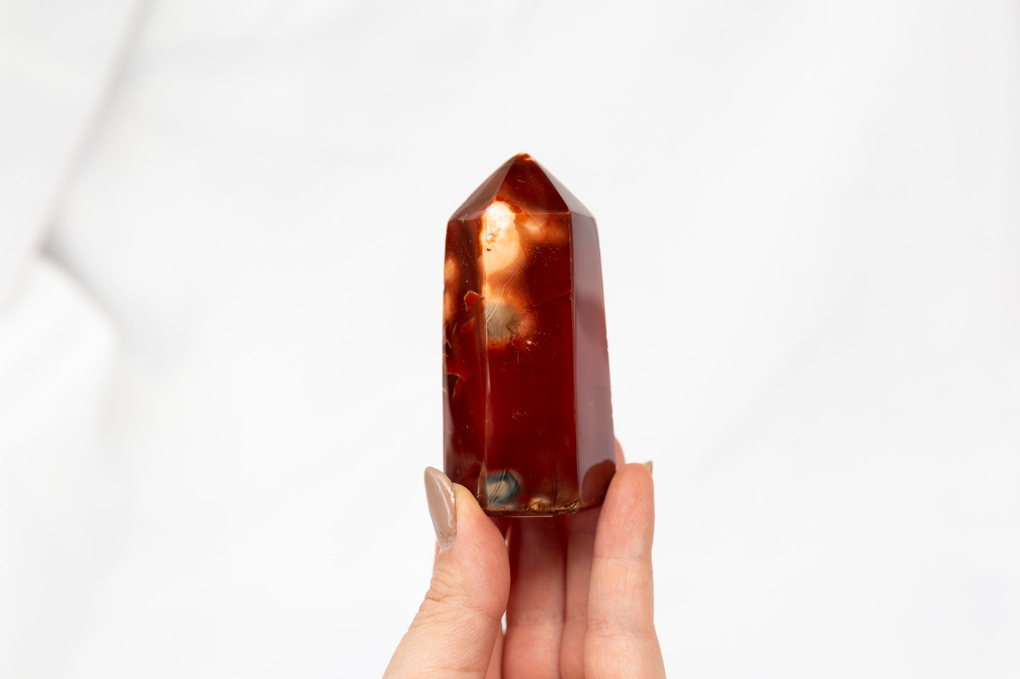 Hand holding a polished red crystal against a white background