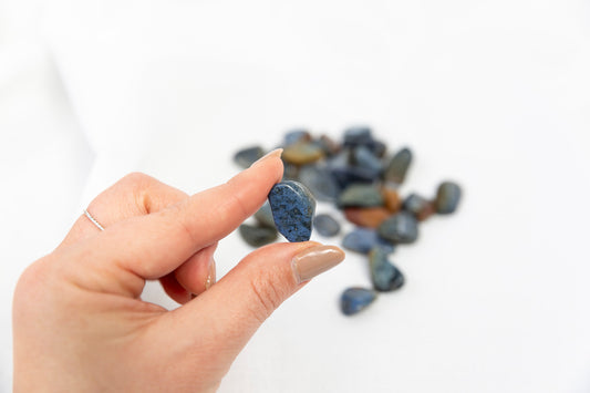 Hand holding a small blue stone with a pile of stones in the background on a white surface