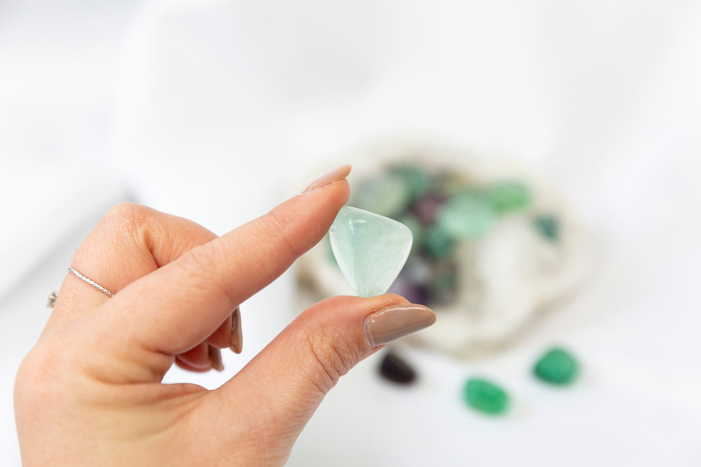 Hand holding a clear green crystal with blurred background