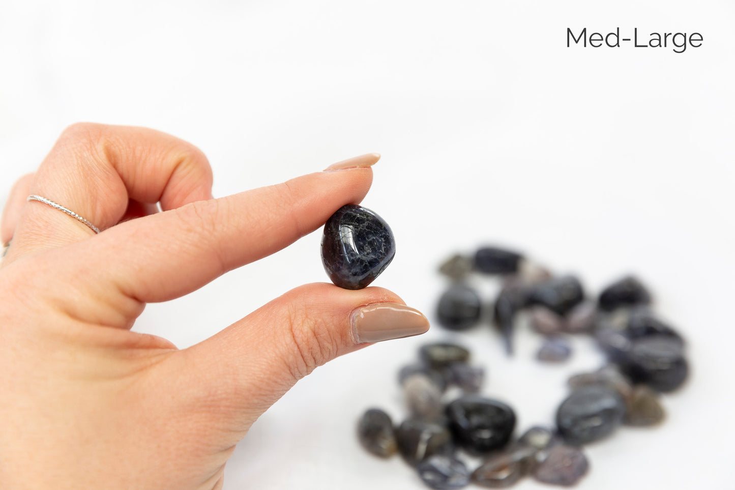 Hand holding a dark stone with a pile of stones on a white background