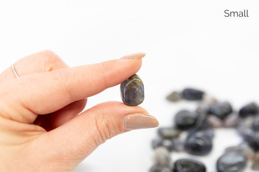 Hand holding a small stone with a blurred pile of stones in the background