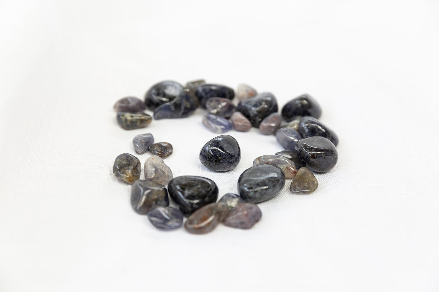 Round iolite tumblestones arranged in a circle on a white background