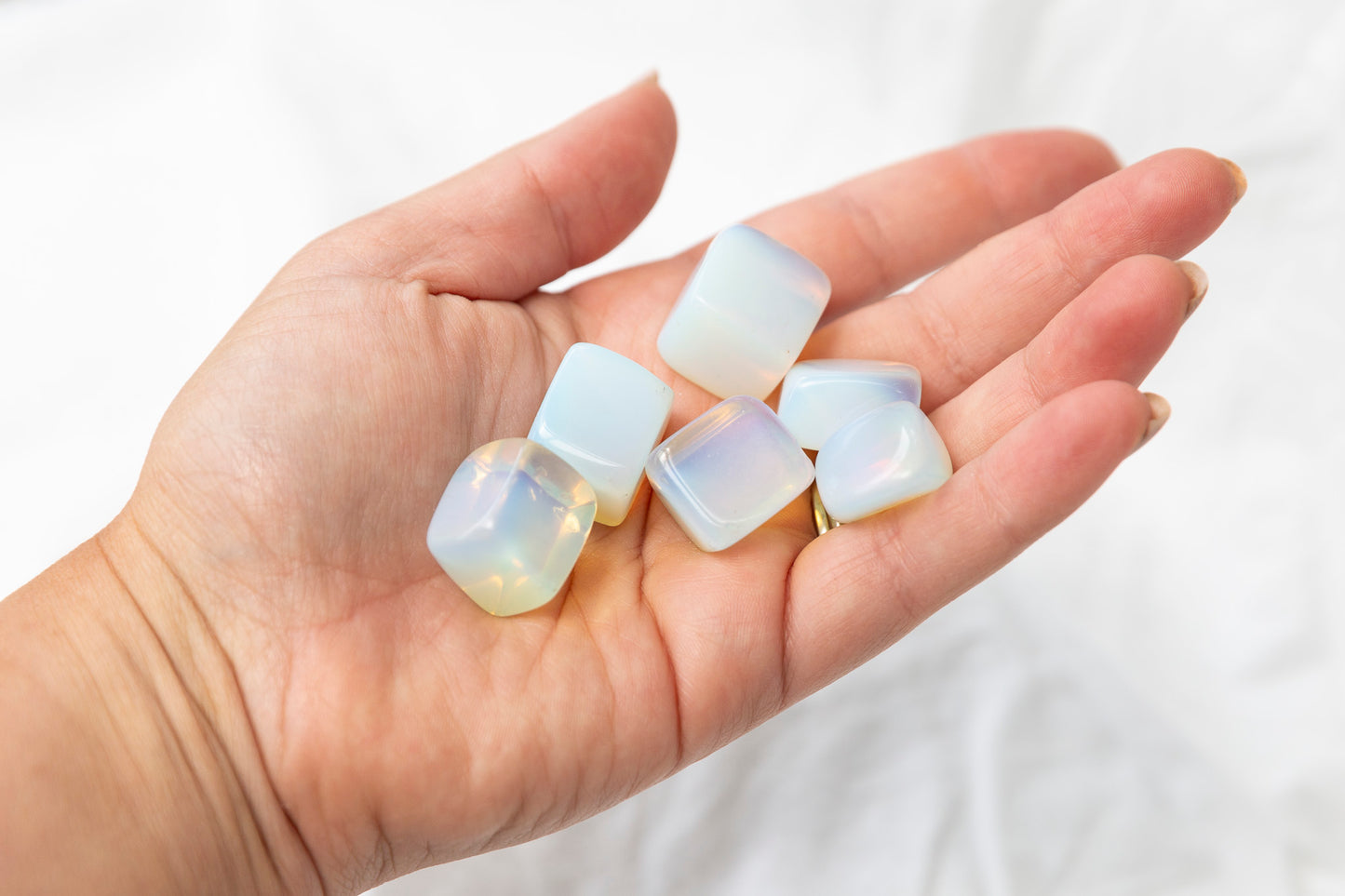 Hand holding translucent opalite tumblestones against a white background