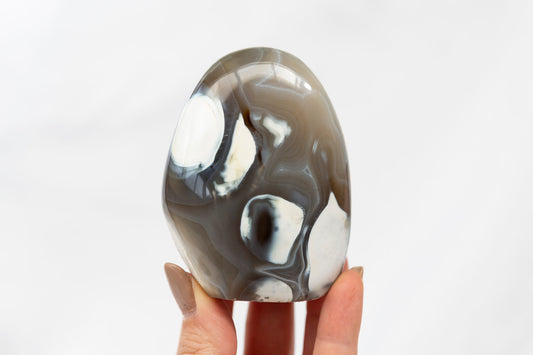 Orca agate freeform held by a hand against a white background