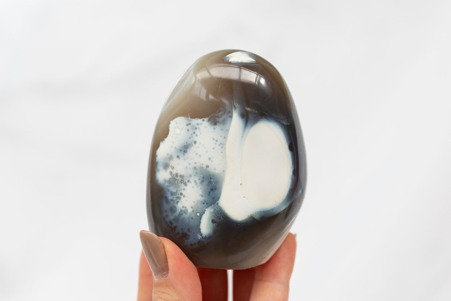 Orca agate freeform held by a hand against a white background