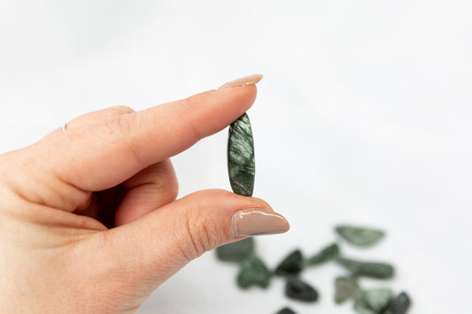 Hand holding a green stone with more stones in the background on a white background