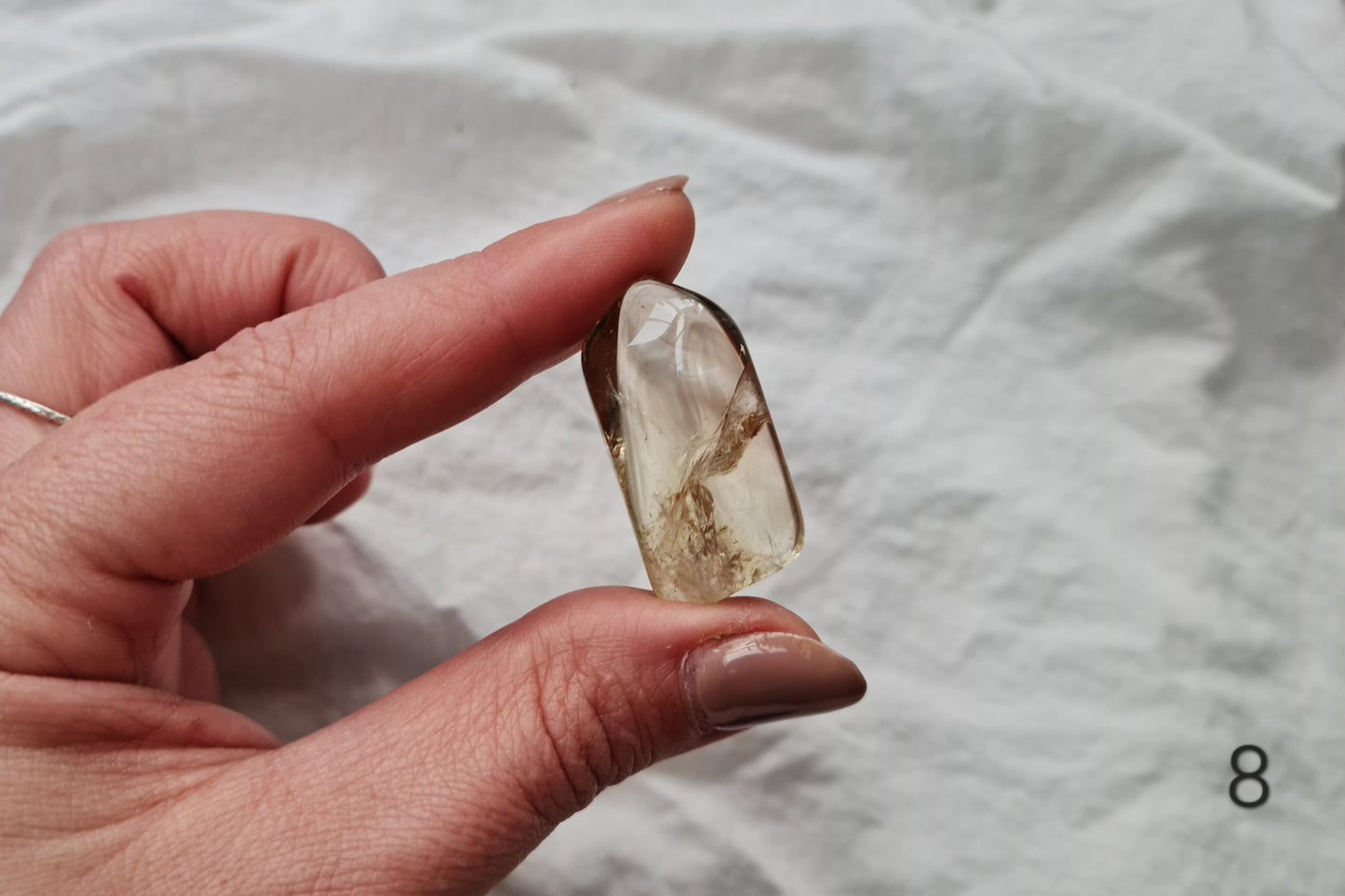Hand holding a citrine crystal tumblestone against a white fabric background