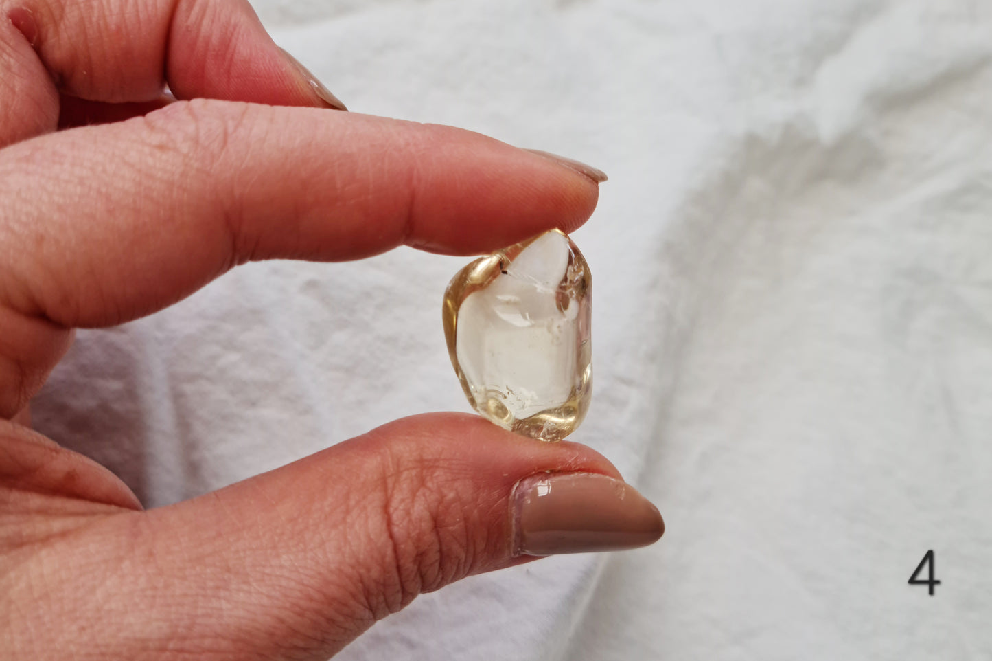Hand holding a citrine crystal tumblestone against a white fabric background
