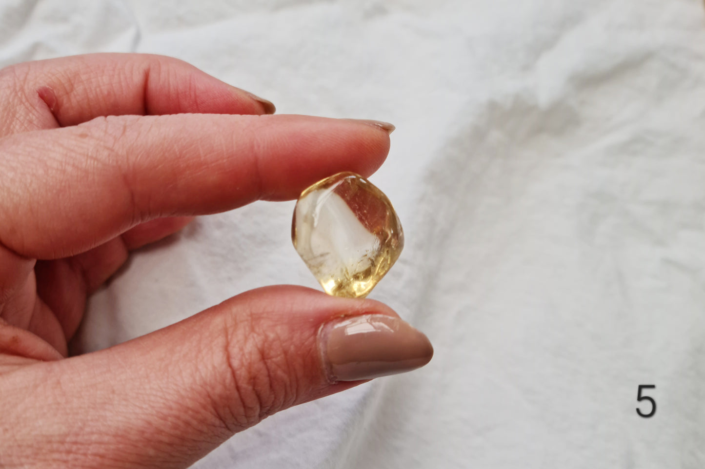 Hand holding a citrine crystal tumblestone against a white fabric background