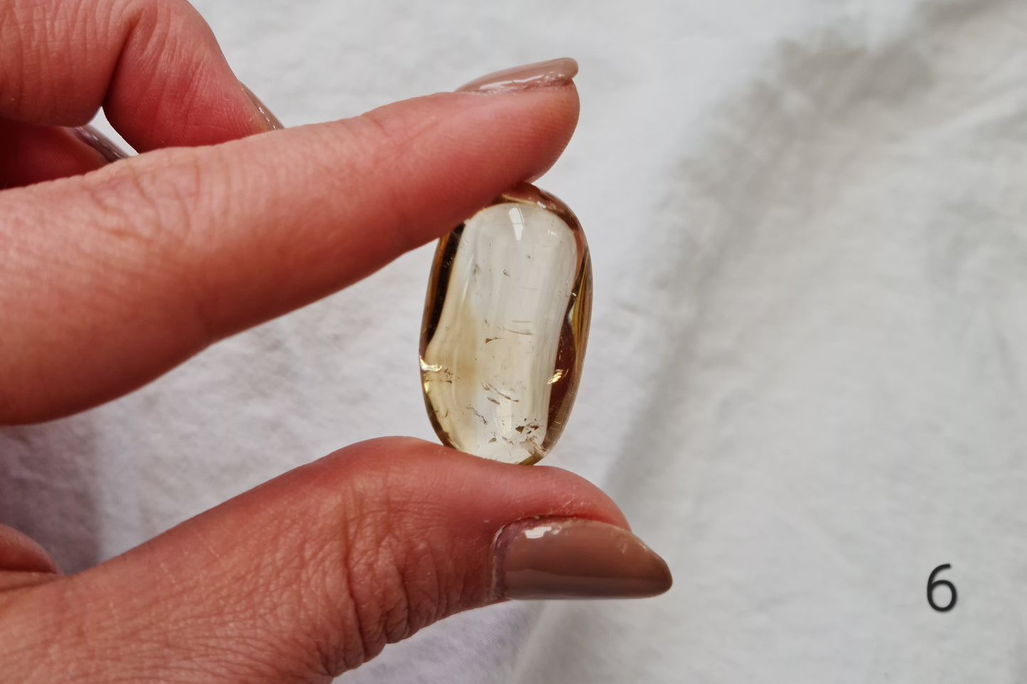 Hand holding a citrine crystal tumblestone against a white fabric background
