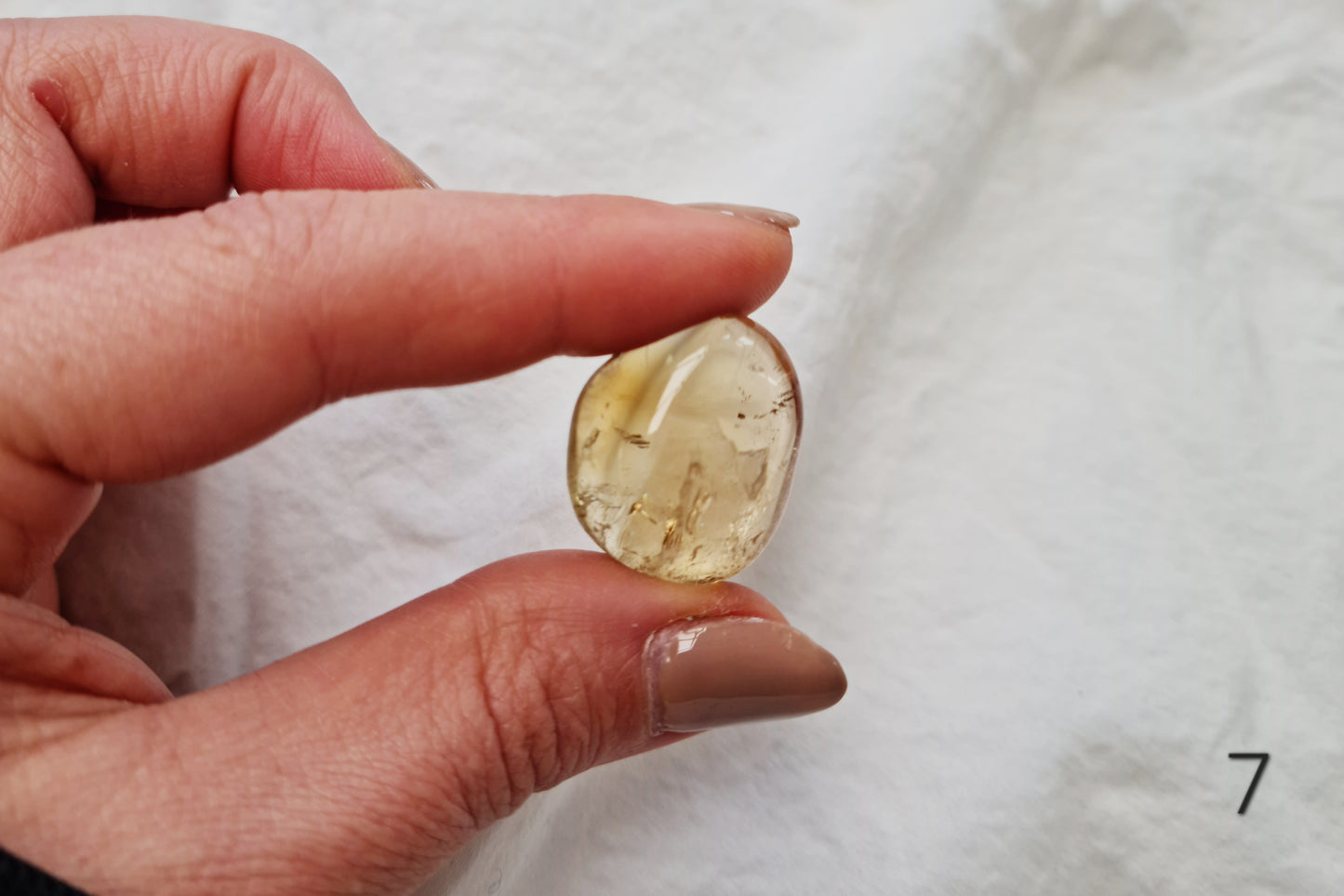 Hand holding a citrine crystal tumblestone against a white fabric background