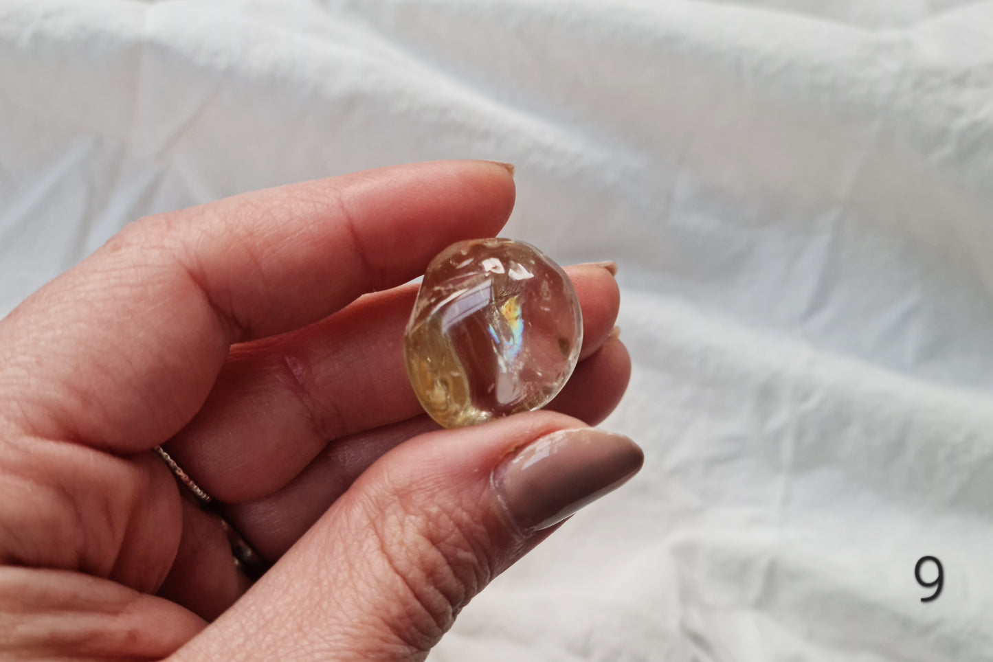 Hand holding a citrine crystal tumblestone against a white fabric background