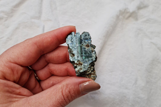 Hand holding a vivianite crystal specimen against a white fabric background