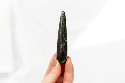 Hand holding a long, dark stone tool against a white background