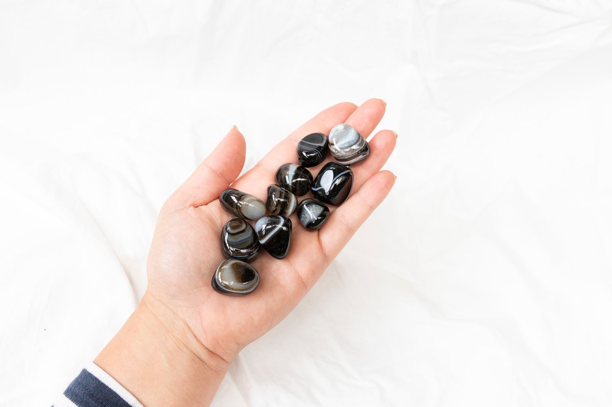 Hand holding black agate tumblestones against a white background