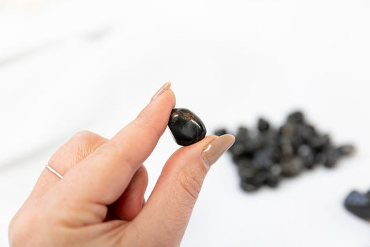 Hand holding a small black stone with more stones in the background on a white surface
