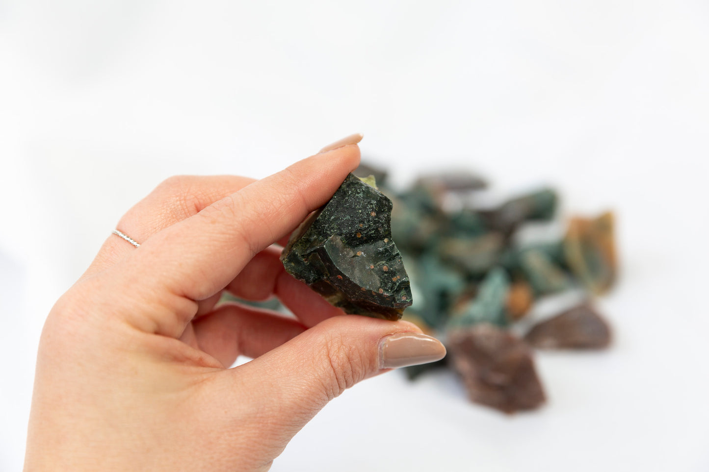Hand holding a dark green crystal with more crystals in the background on a white surface
