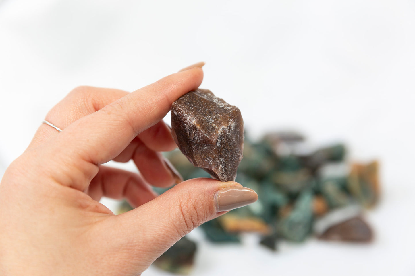Hand holding a rough brown stone with more stones in the background on a light background
