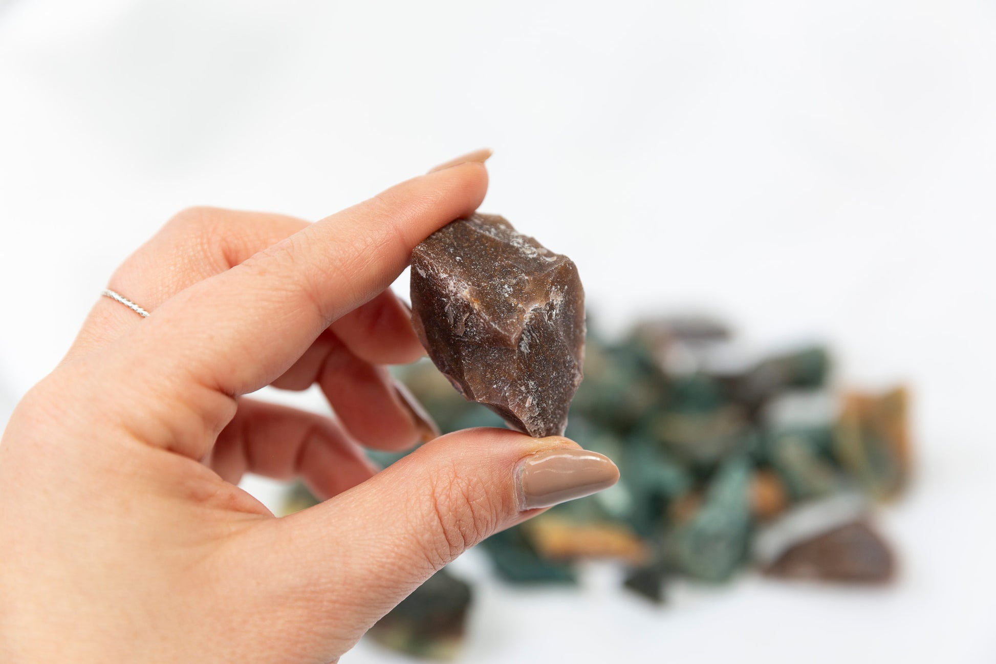 Hand holding a rough brown stone with more stones in the background on a light background