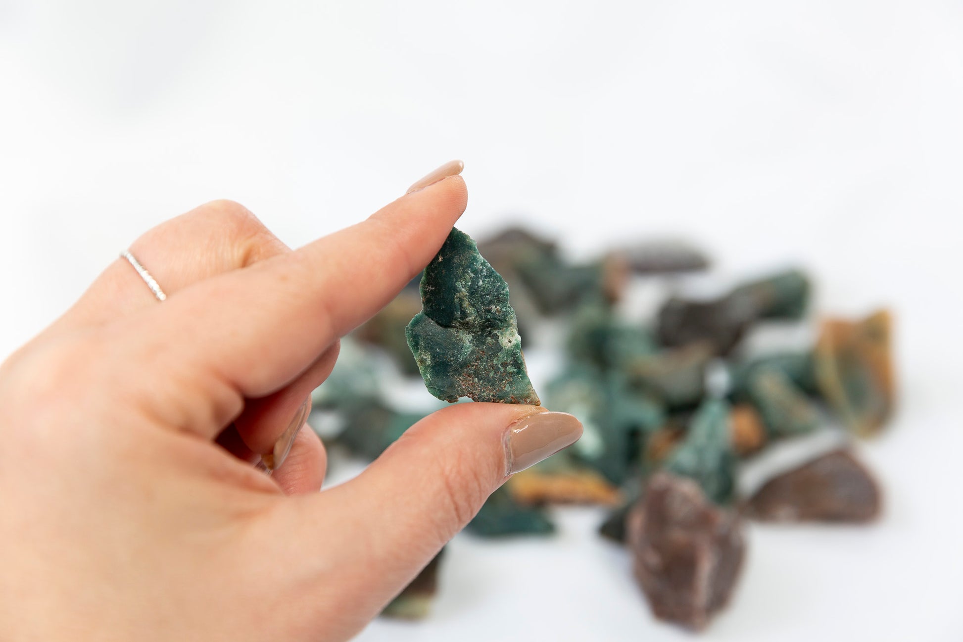 Hand holding a green crystal with more crystals in the background on a white surface