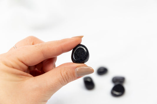 Hand holding a small blue goldstone crystal with more stones in the background on a white surface