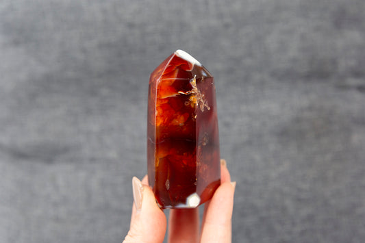 Hand holding a reddish orange crystal against a grey background