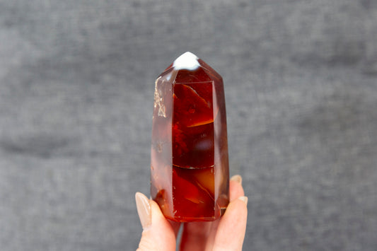 Hand holding a reddish orange crystal against a grey background