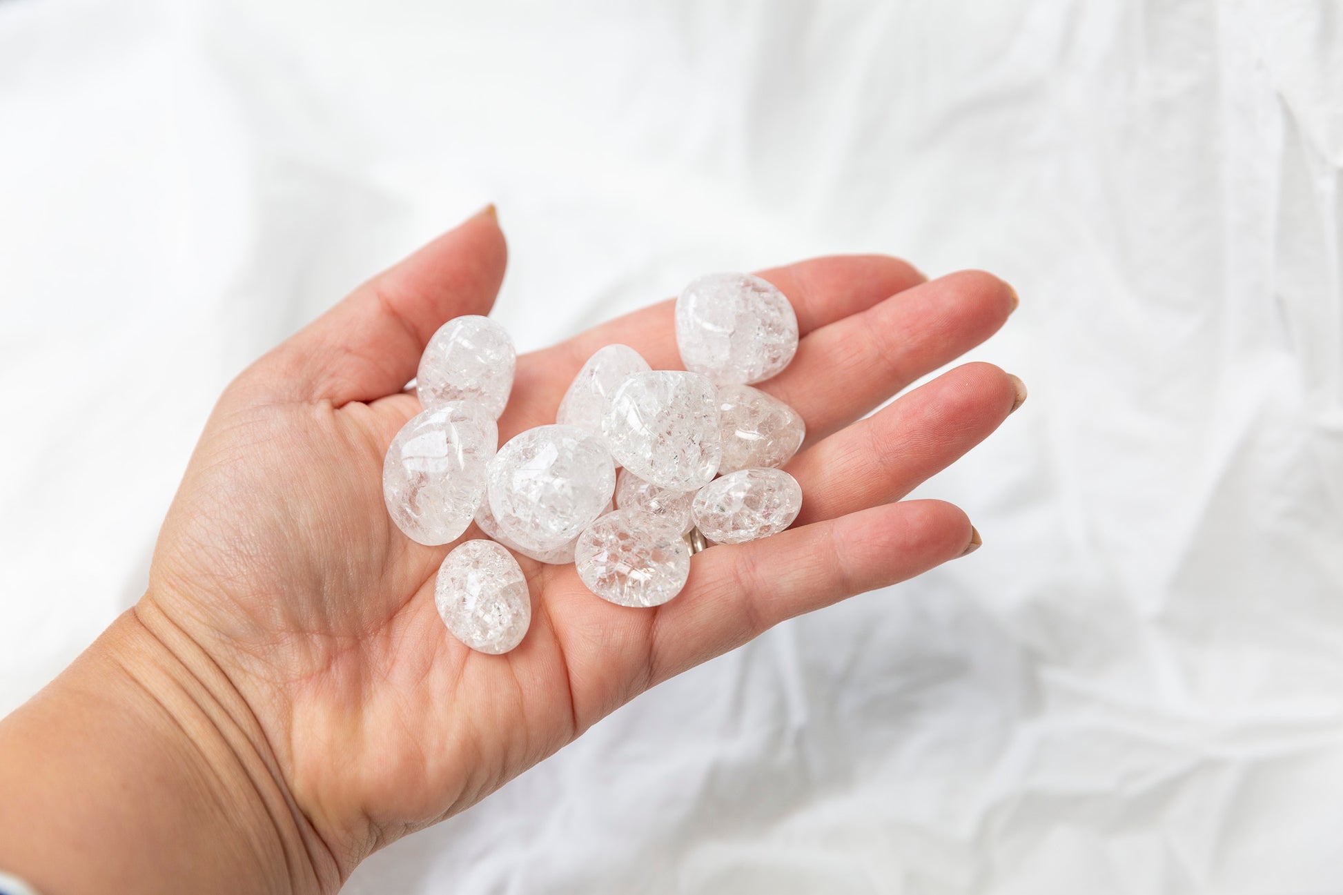 Hand holding crackled quartz tumblestones against a white background