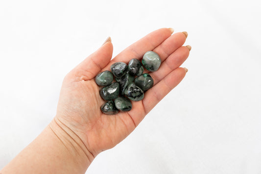 Hand holding a small pile of dark green stones against a white background