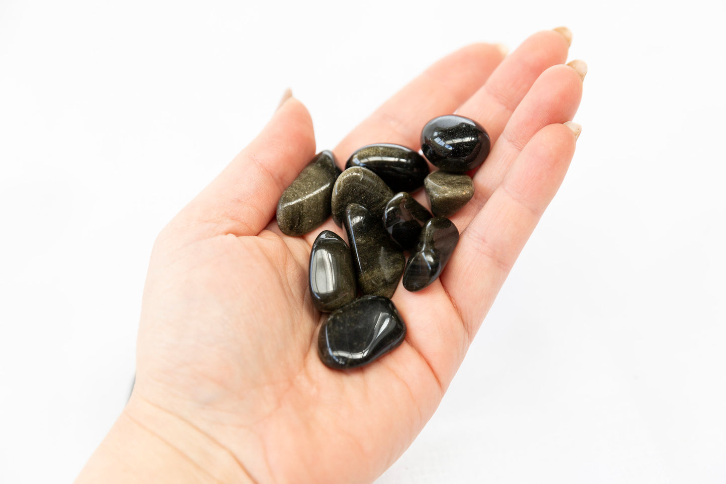 Hand holding a small pile of polished black stones on a white background