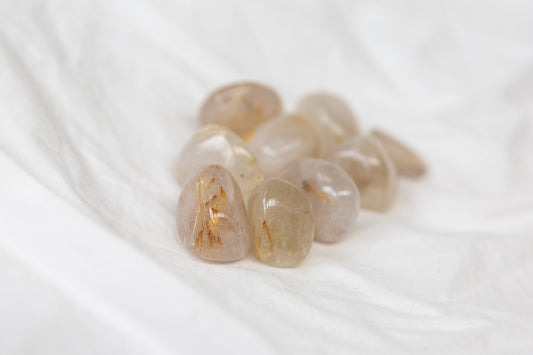 Severl golden rutilated quartz tumblestones on a white background