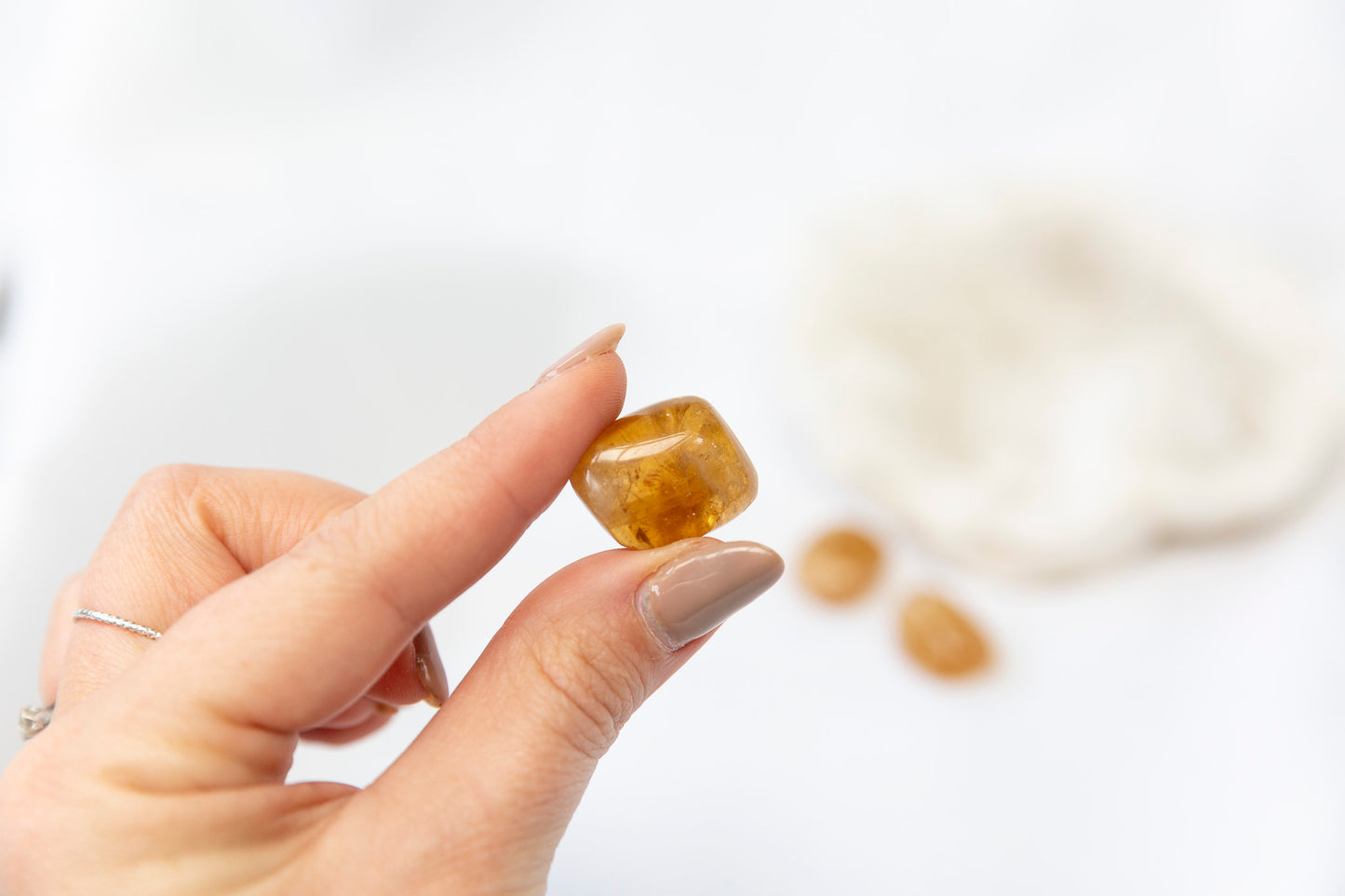 Hand holding a small honey calcite tumblestone against a blurred background