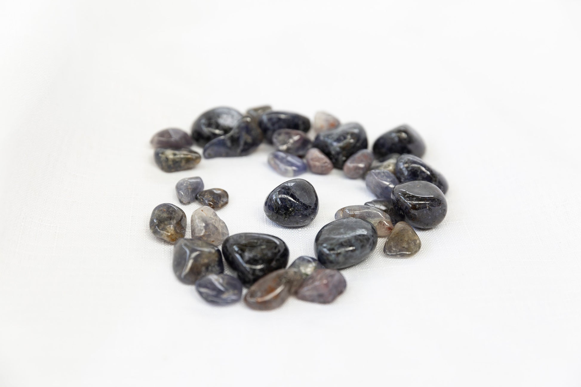 Round iolite tumblestones arranged in a circle on a white background