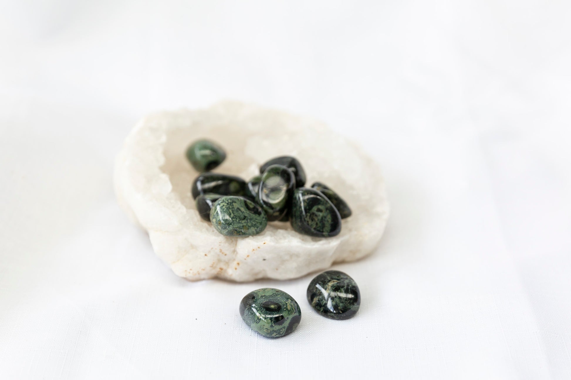 Green stones on a clear quartz geode against a white background