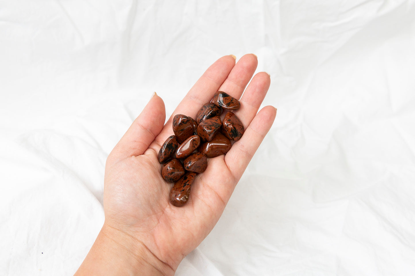 Hand holding red and black mahogany obsidian tumblestones against a white background