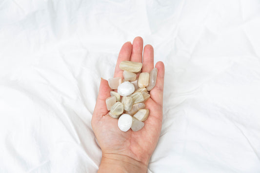 Hand holding a small pile of white moonstone tumblestones against a white background