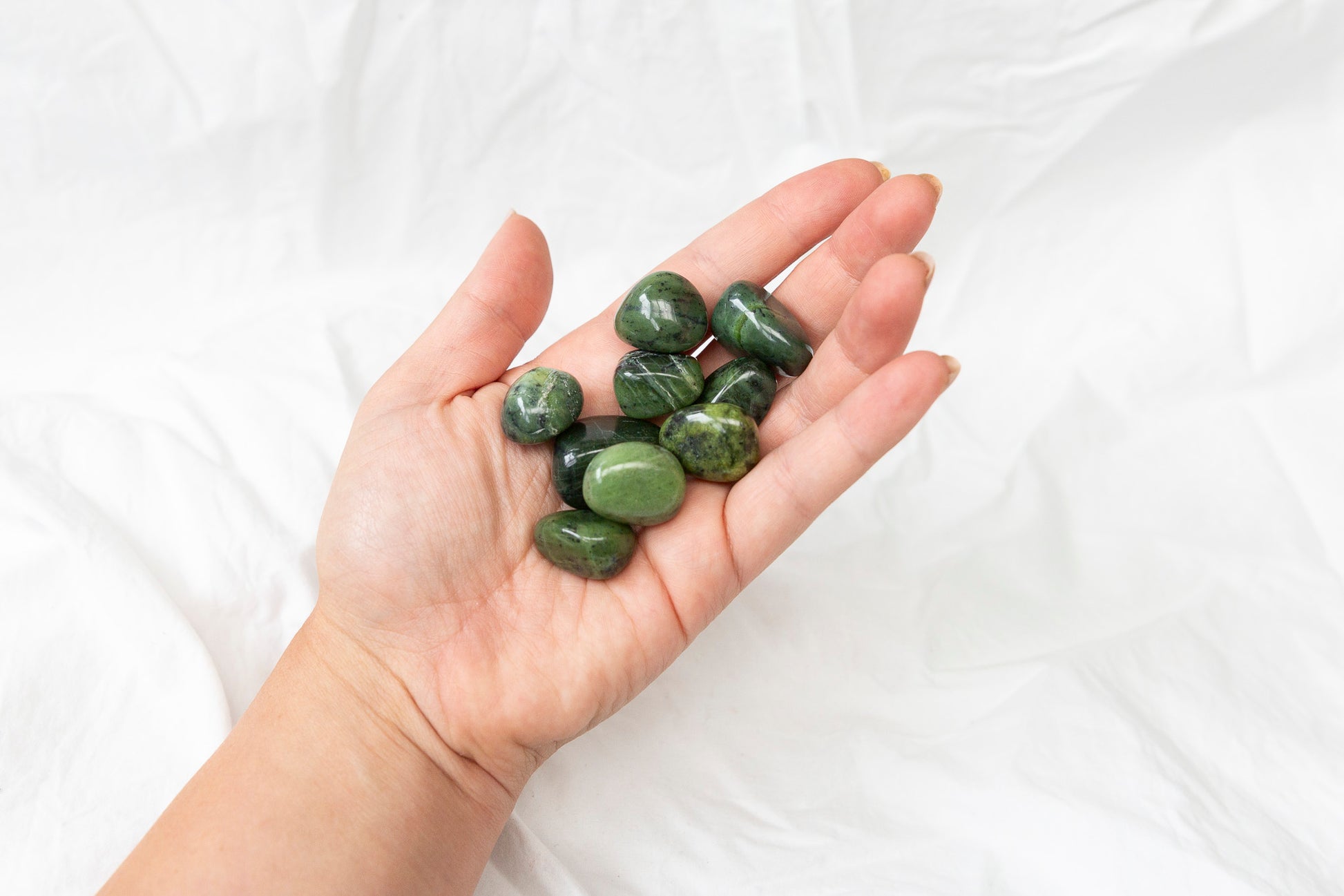 Hand holding green jade crystal tumblestones against a white background