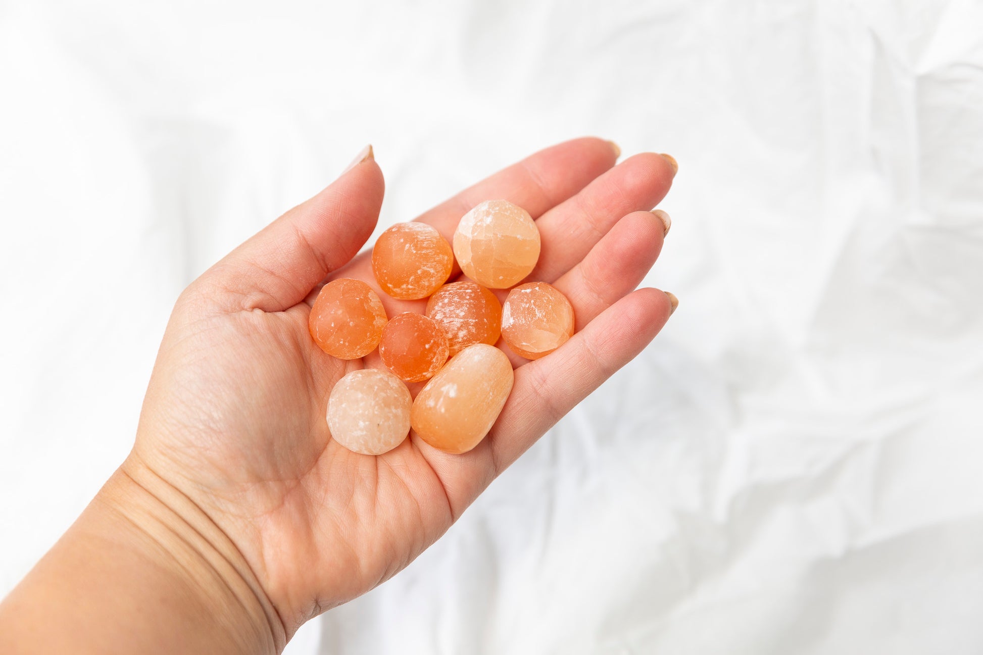 Hand holding orange satin spar tumblestones against a white background