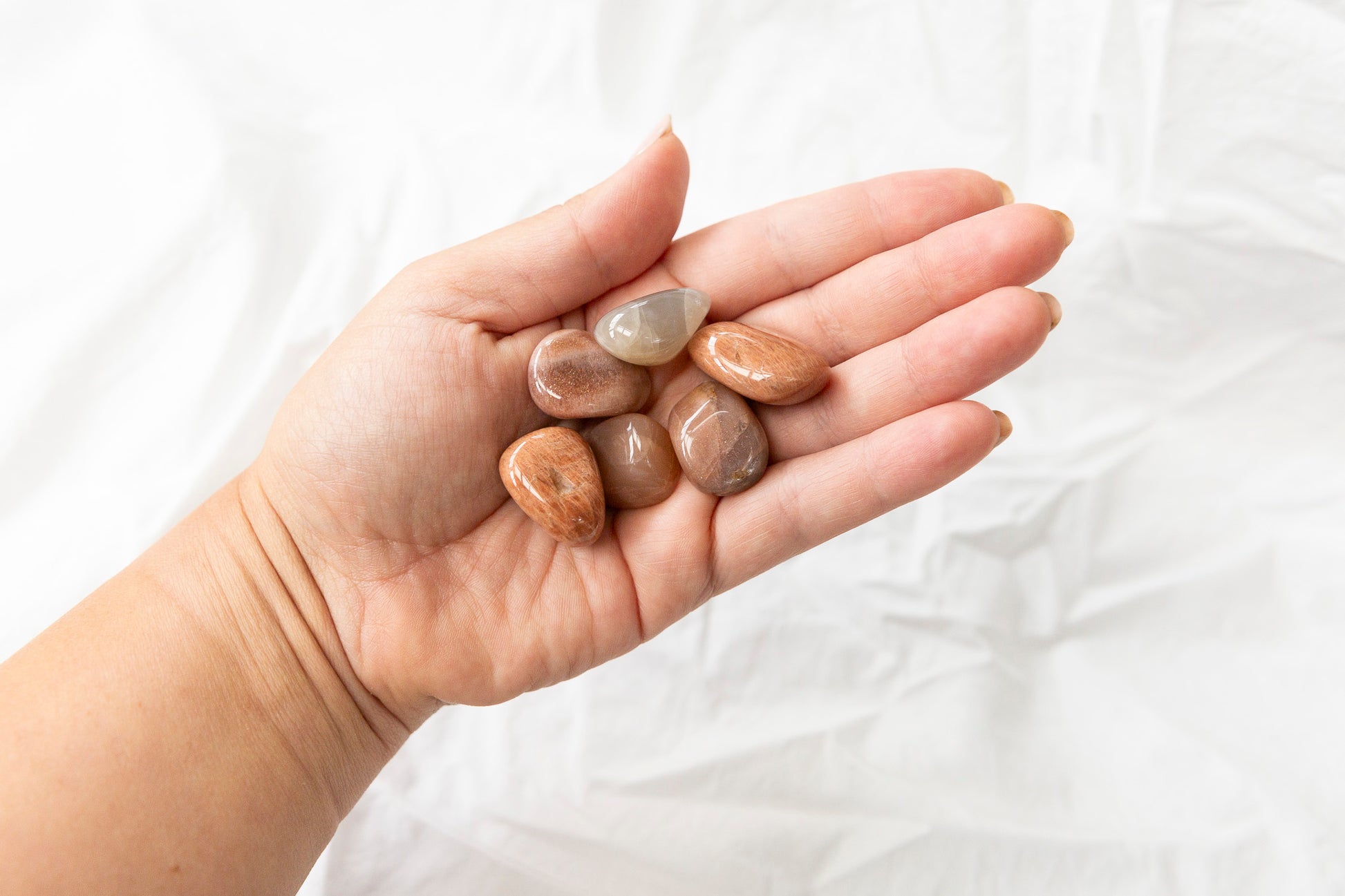Hand holding small peach moonstone crystals against a white background