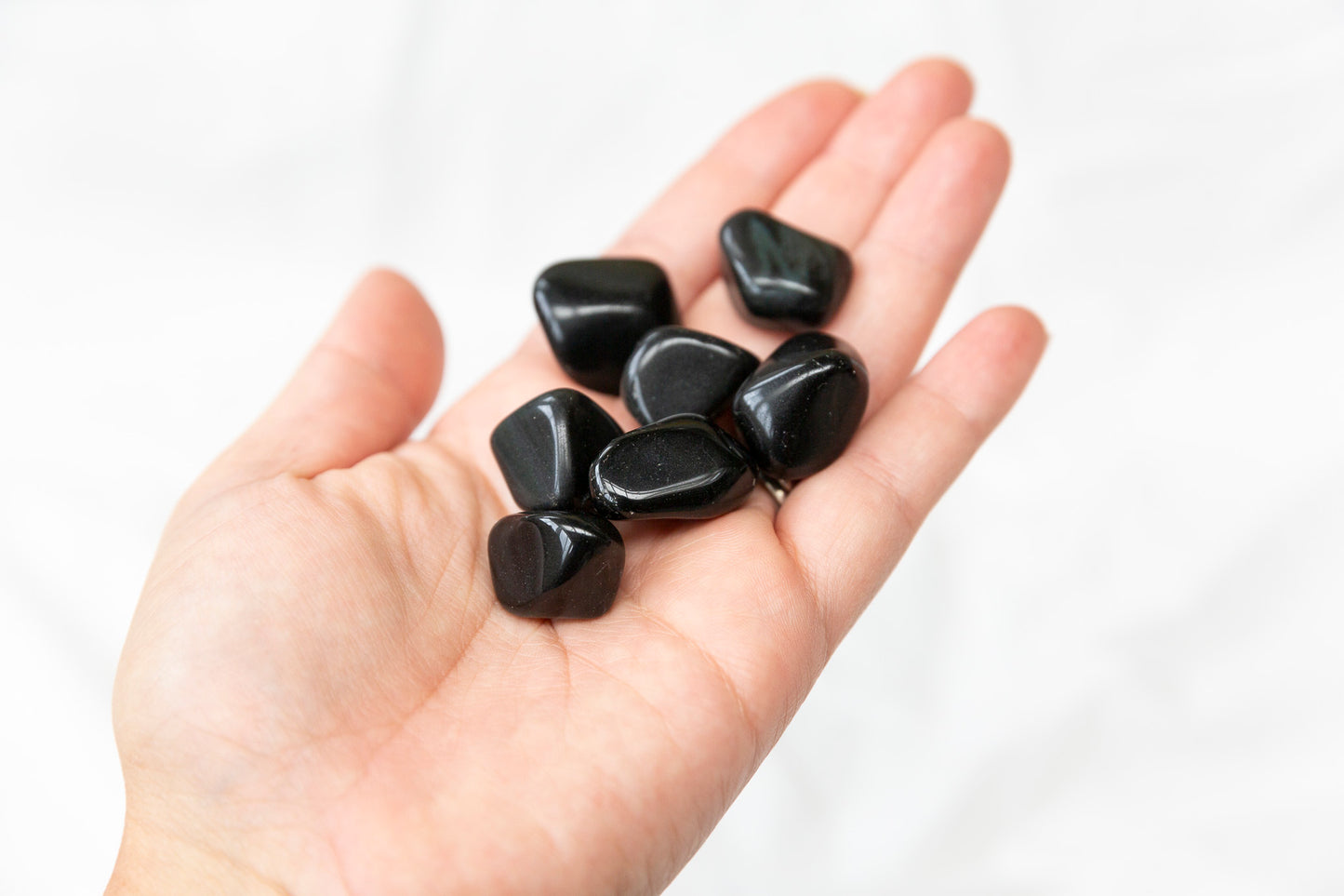 Hand holding rainbow obsidian tumblestones against a white background