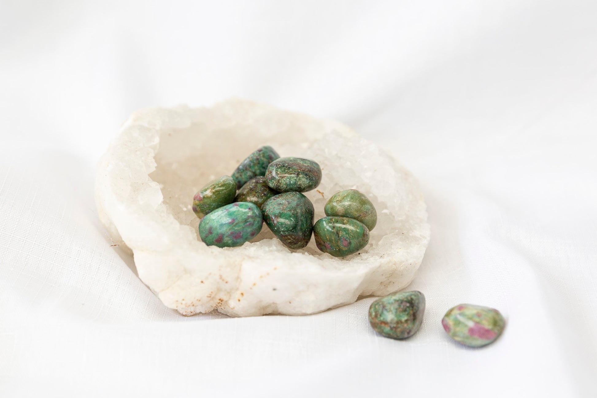 Green and pink ruby fuchsite tumblestones on a clear quartz geode with a white background