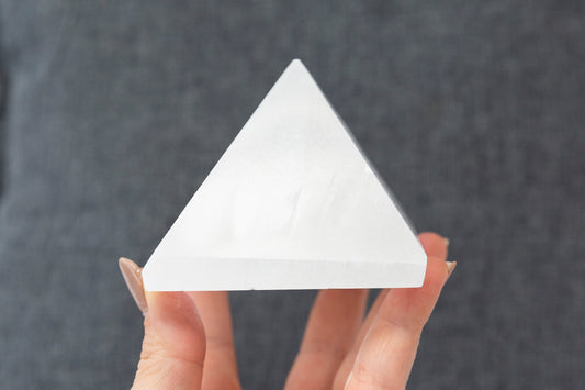 Hand holding a white pyramid-shaped crystal against a dark background